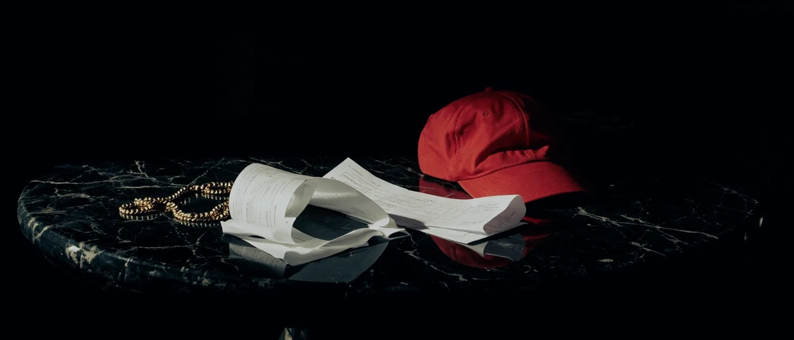 Casquette rouge et ticket de caisse sur marbre sombre, clair-obscur